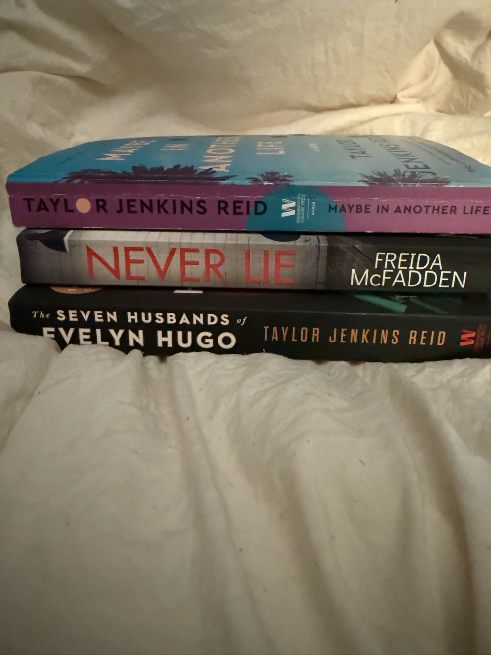 Stack of Three Paperback Novels – Blue, Purple, Black Spines